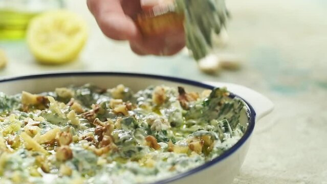 Piece of bread is dipped in spinach and yogurt dip with walnuts.
