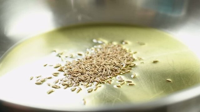 The cook adding cumin seeds into frying pan with olive oil.
