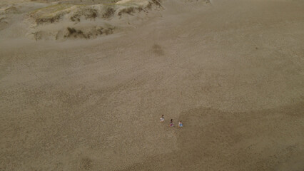 Three friends walking on beach with deck chairs at sunset, Playa La Viuda in Uruguay. Aerial top-down view