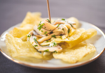 Potato chips with pickled anchovies in a white round plate on a table. Typical Spanish food called “tapa” to eat in a bar.