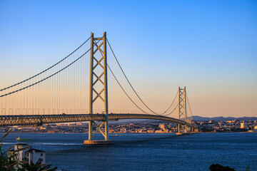 Small boats under iconic Akashi suspension bridge at sunset