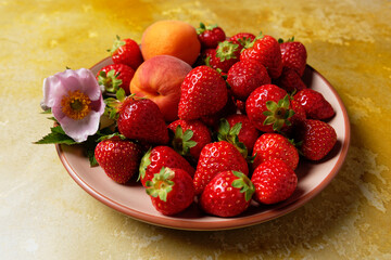 A group of ripe red strawberries and two apricots served on a plate. Selective focus.