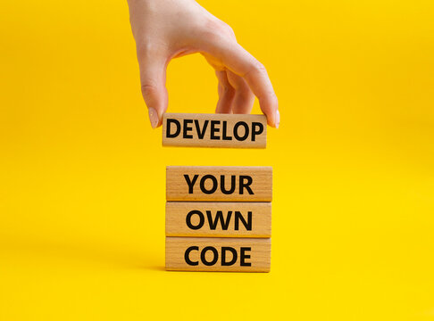 Develop your own code symbol. Concept words Develop your own code on wooden blocks. Beautiful yellow background. Businessman hand. Business and Develop your own code concept. Copy space.