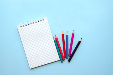 white blank opened notebook and school supplies on blue background. White sheet of paper, colored pencils. Back to school. Copy space