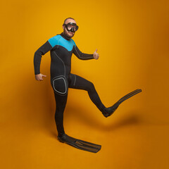 Fototapeta na wymiar Happy scuba diver diving man going to the side against bright orange studio wall background