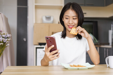 Home relaxation concept, Young woman eating crackers and surf social media on smartphone at home