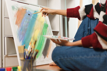 The art concept, Asian female artist sit on the floor and using paint brush to painting on canvas