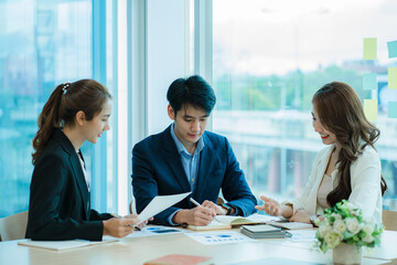 Young Asian business team working with laptops on financial documents with happy smiles. Group of business people meeting in a modern office Design and Concept Planning