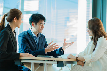 Young Asian business team working with laptops on financial documents with happy smiles. Group of business people meeting in a modern office Design and Concept Planning