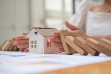 Cropped view of woman hands protecting house model from falling wooden blocks. Risk prevention,...