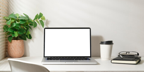 Bright modern working space with laptop, potted plant, coffee cup and notebook. White screen for your advertise text.
