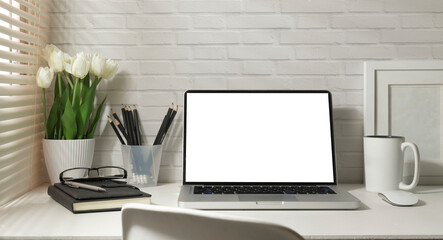 Laptop, picture frame, stationery and vase with bouquet of beautiful tulips on white table.