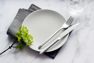 Elegant table setting with empty grey plate, silver cutlery on linen napkin. Table decoration.