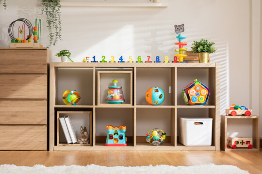 Interior of baby or child room with toys in cozy and warmth home. Nursery room with colorful toys in wooden box for development baby skill with morning light. Comfortable living room for kid and baby