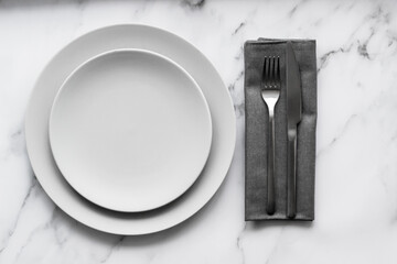 Dining table setting. Two grey plates with silver cutlery on the linen napkin.