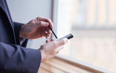 Businessman hands using smartphone and stylus near window in office close up