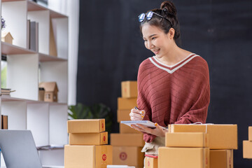 SME Online seller Young Asian woman freelance working on laptop and box, checking online order orders from customers delivery package shipping postal SME entrepreneur online business 