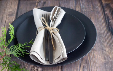 Rustic table setting with black empty plate, black cutlery and linen napkin on the wooden table. Dining setting.