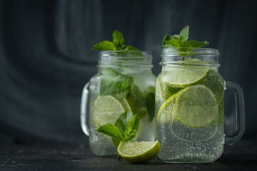 Refreshment mojito cocktail with mint and lime in a glass mug on a black background. Cold summer drink with ice