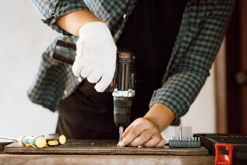 Close up of male mechanic holding electric cordless screwdriver drill with wood screw in the factory. Working with the screw. Professional carpenter. Concept furniture at home. - obrazy, fototapety, plakaty