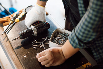 Close up of male mechanic holding electric cordless screwdriver drill with wood screw in the factory. Working with the screw. Professional carpenter. Concept furniture at home.