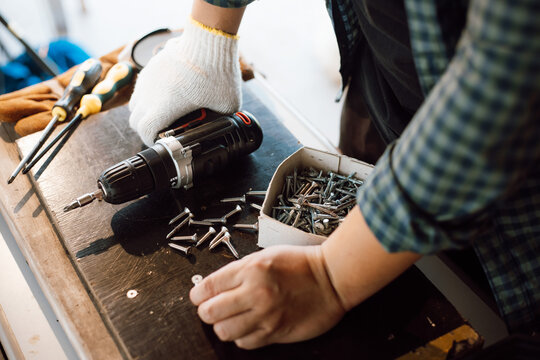 Close Up Of Male Mechanic Holding Electric Cordless Screwdriver Drill With Wood Screw In The Factory. Working With The Screw. Professional Carpenter. Concept Furniture At Home.