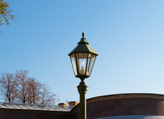 Fototapeta na wymiar Old vintage black decorative lantern on pillar. Blue sky on a sunny day. Saint Petersburg city park in autumn sun light