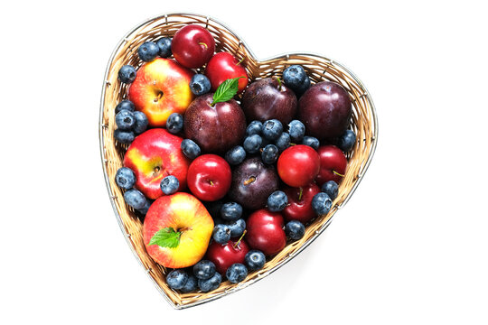 Fruit for the Jewish New Year. Red apples and plums in straw basket made in the shape of heart on white background.