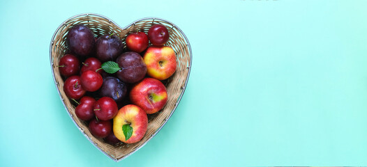 Fruit for the Jewish New Year. Red apples and plums in straw basket made in the shape of heart on green background.