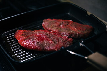 Closeup shot of metal skillet with piece of fresh meat and hot oil standing on modern stove surface