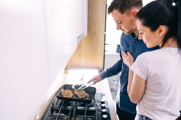 cute couple hugging in the kitchen while cooking steak for dinne