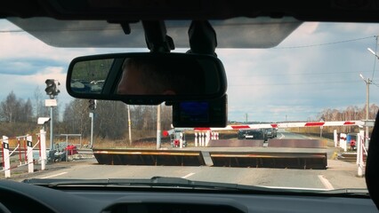 View from the front window of a car at a railway crossing with a lowered barrier and raised...