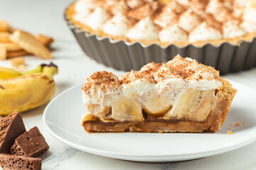 Banoffee cake with banana and caramel sauce filling sprinkled with grated dark chocolate on the white marble background. English traditional pie © alexanderon