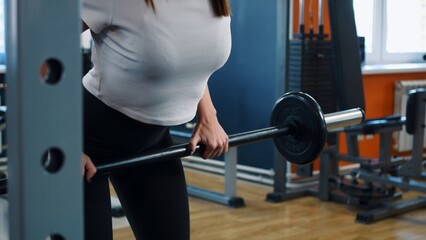 Fototapeta na wymiar A young woman is engaged in a fitness club according to an individual program. A woman performs a straight-grip barbell row. Exercise is used to develop the back muscles. Woman doing sports exercises.