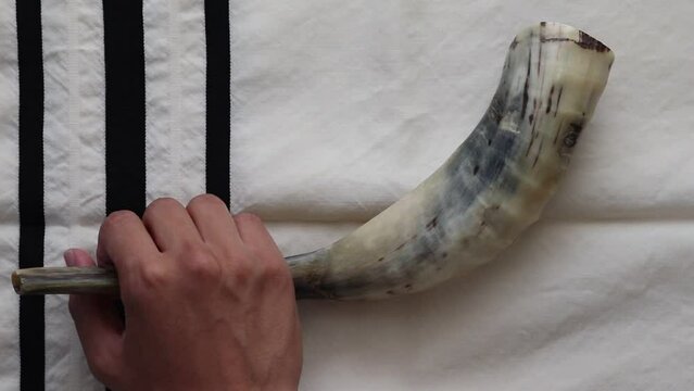 A boy's hand holds a shofar on a tallit background
