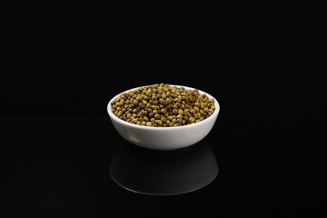 Coriander fruit in a white plate on a dark table with reflection. Close-up