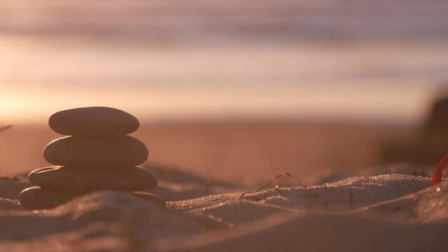 Stack of pebble stones, sandy ocean beach, sunset sky. Rock balancing in sun light, sea water waves. Stones staking in pyramid pile. Zen meditation and harmony in balance. Seamless looped cinemagraph.