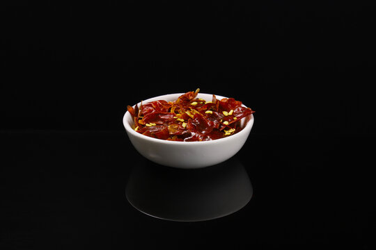 Dried red chili peppers in a white plate with reflection on a dark table. Close-up