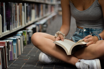 Young girl sitting on floor at library reading book
