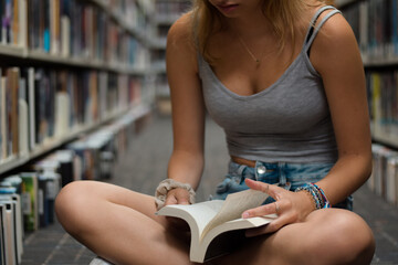 Young girl sitting on floor at library reading book