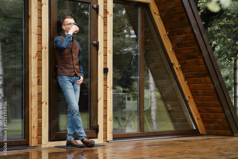 Wall mural confident middle age man stands on the terrace of a forest chalet leaning against glass door