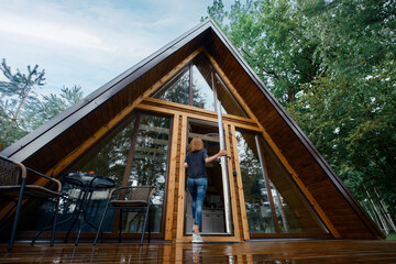 Woman opens the door of a forest chalet and enters inside, back view