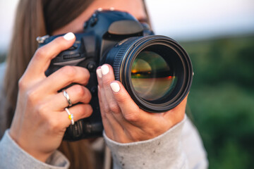 A young woman with a professional camera takes a photo in nature.