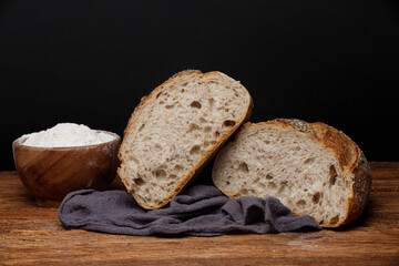 Two halves of artisan sourdough bread with poppy seeds and sesame seeds on a linen towel on a wooden table. Homemade wheat bread cut in half