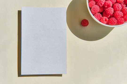 Summer rural still life. Greeting mockup scene on beige background.Blank paper, cup with raspberries