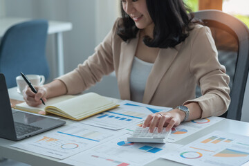 Portrait of a female accountant using a calculator and laptop to calculate balance using graphs for customers.