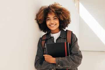 Portrait of a young beautiful female student leaning a wall. Smiling girl looking at camera while standing in high school. - Powered by Adobe
