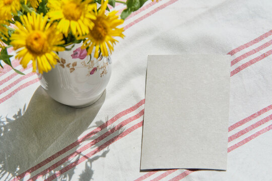 Greeting mockup scene on striped cotton napkin. Blank paper, bouquet of yellow wild meadow flowers