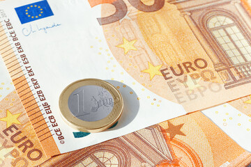 One EU euro coin on heap of 50 euro bills. EU economy and finance. Cash money. Currency background. Close up view.