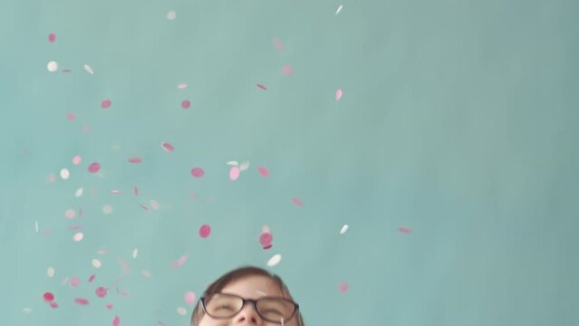 Slowmo of happy little girl with down syndrome throwing confetti in air and smiling at camera standing on light blue studio background